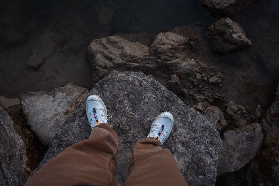Top-down view of man’s sneakers on a rocky cliff edge, showcasing outdoor footwear style.