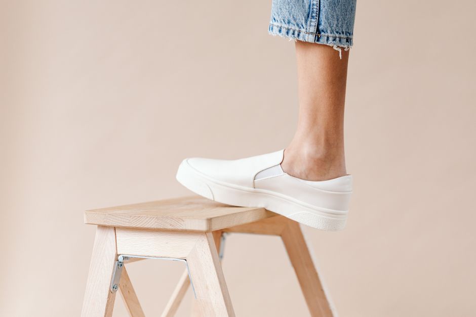 Close-up of a foot in white sneakers on a wooden stool, minimalist setting.