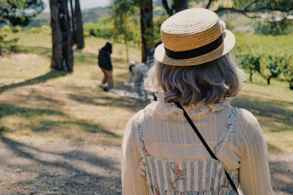 A woman in floral dress and straw hat enjoys a sunny picnic outdoors with friends.