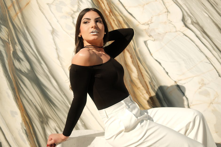 Elegant fashion portrait of a woman in monochrome attire posing against a marble backdrop.