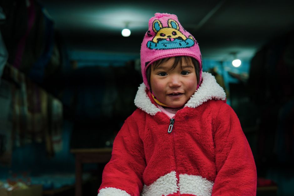Adorable child wearing a vibrant red winter coat and knit hat smiles indoors.