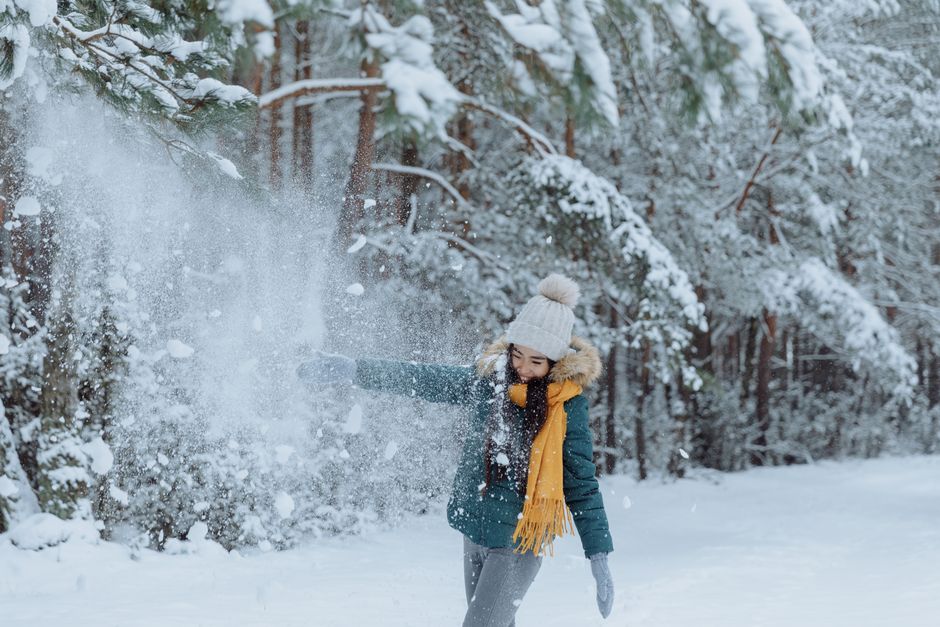 Woman in winter clothing enjoying snow in a forest, capturing the essence of playful winte