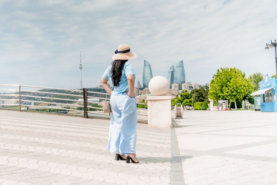 A woman in a sunhat and blue dress stands overlooking Baku's skyline with the iconic Flame Towers.